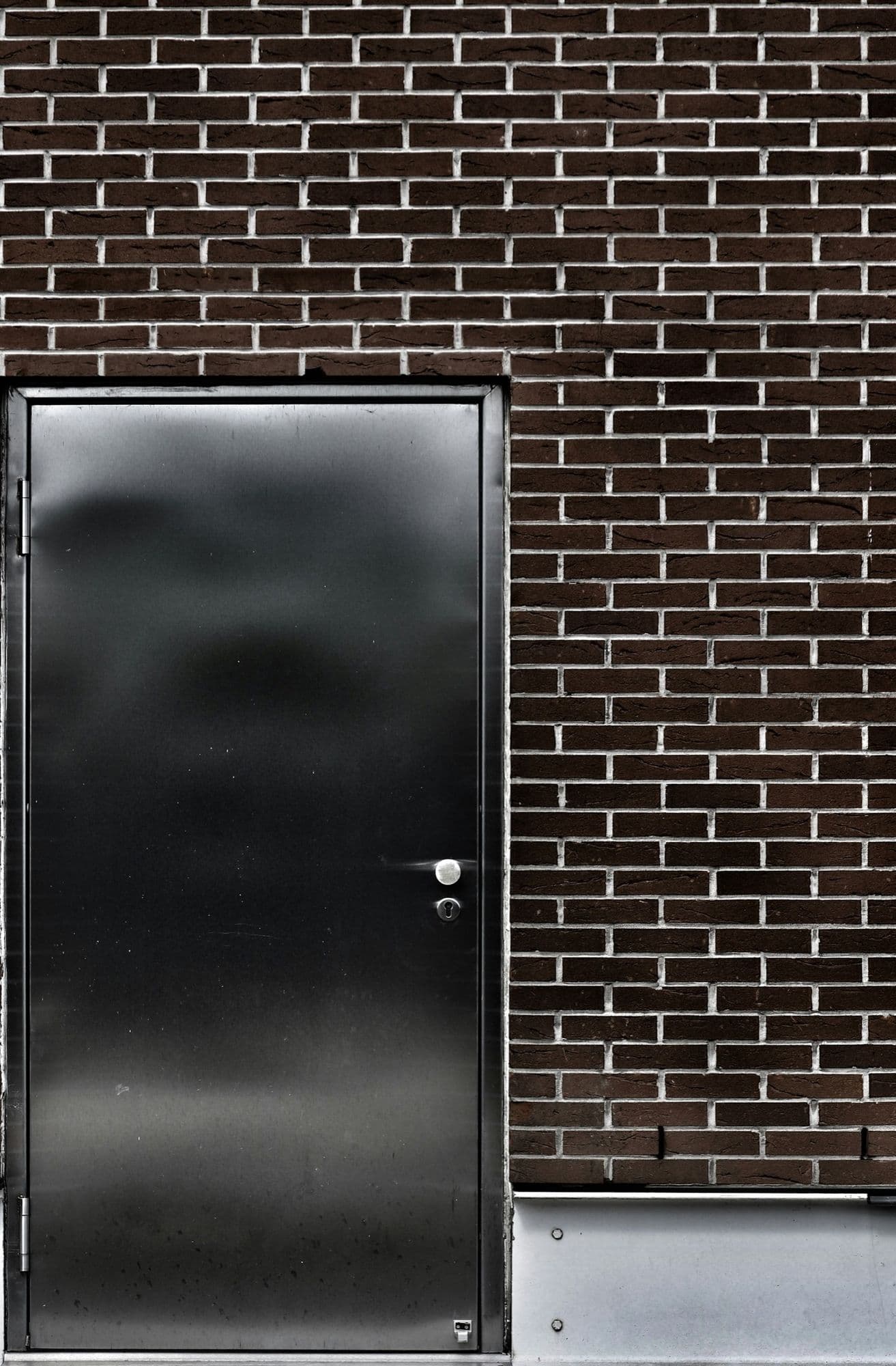 A black steel door in a dark brick wall